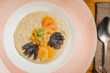 Oatmeal porridge with dried fruits and spoon on wooden table