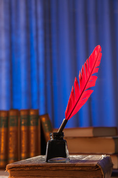 Red quill pen and black inkwell on an old book on a blue background