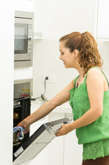Fototapeta na wymiar Woman wearing green top in modern kitchen holding mittens and