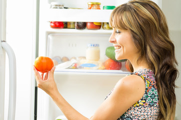 Woman wearing colorful dress in modern kitchen opening fridge