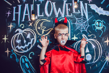 Boy in a Dracula costume posing on the background of the inscription Halloween