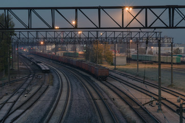 Illuminated cargo train station by night. Curve platform with containers