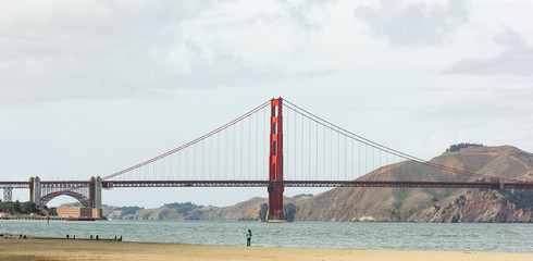 A woman stand on the beach and looking at Golden Gate bridge.