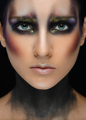 Makeup art and beautiful model theme: beautiful girl with a creative make-up black-and-purple and gold colors on a black background in the studio