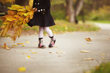 Warm stylish autumn boots. Fall foliage and warm clothes. Girl holding yellow leaves bouqet on a autumn day.