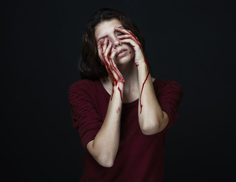 Scary Girl and Halloween theme: portrait of a crazy girl with a bloody hand covers the face in studio on a dark background, bloody tears