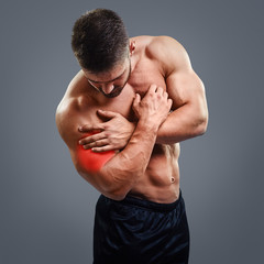 Muscular shirtless man with biceps pain over gray background. Concept with highlighted glowing red...