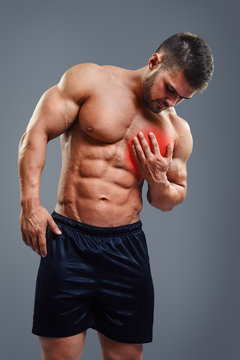 Muscular shirtless man with chest pain over gray background. Concept with highlighted glowing red spot.