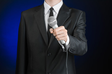 Business and speech topic: Man in black suit holding a microphone on a gray dark blue isolated...