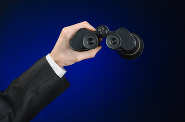 Business and search topic: Man in black suit holding a black binoculars in hand on a dark blue background in studio isolated