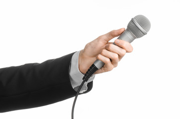 Business and speech topic: Man in black suit holding a gray microphone on an isolated white...