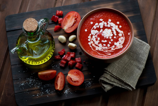 Gazpacho and its ingredients on a rustic wooden cutting board