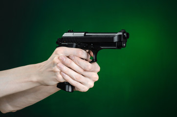 Firearms and murderer topic: human hand holding a gun on a dark green background isolated in studio