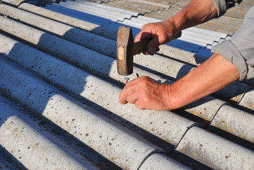 Repair dangerous asbestos old roof tiles. Roofer installs asbestos roof shingles - closeup on...