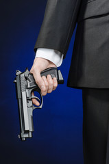 Firearms and security topic: a man in a black suit holding a gun on a dark blue background in studio isolated