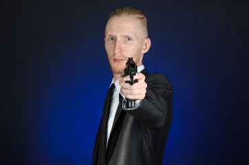 Firearms and security topic: a man in a black suit holding a gun on a dark blue background in studio isolated