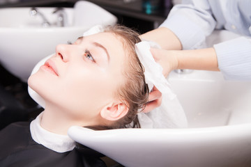 Stylist drying woman hair with towel in salon