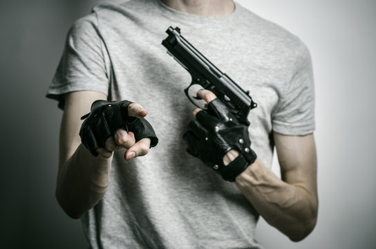 Horror and firearms topic: the killer with a gun in his hand in black gloves on a gray background in the studio
