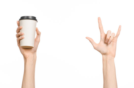 Breakfast And Coffee Theme: Man's Hand Holding White Empty Paper Coffee Cup With A Brown Plastic Cap Isolated On A White Background In The Studio, Advertising Coffee