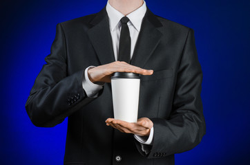 Business lunch and coffee theme: businessman in a black suit holding a white blank paper cup of...