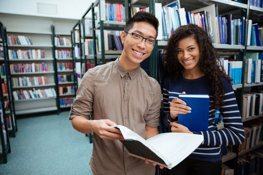 Happy students searching books in library