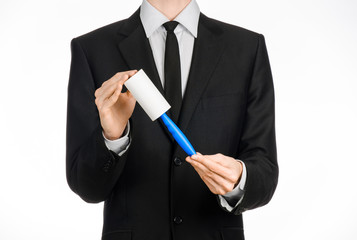 Dry cleaning and business theme: a man in a black suit holding a blue sticky brush for cleaning clothes and furniture from dust isolated on white background in studio.