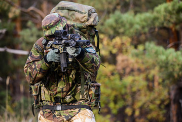 Soldier on battle field in forest, aiming/Armed soldier in uniform with assault rifle in forest...