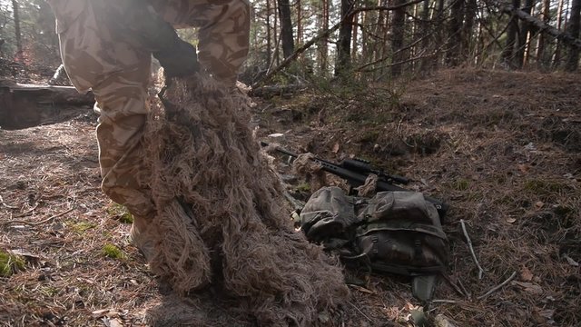 Sniper puts on his camouflage suit/Armed trooper puts on sniper uniform in forest