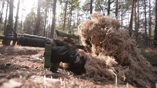 Close-up of sniper in forest/Masked sniper in camouflage aim from assault rifle in forest