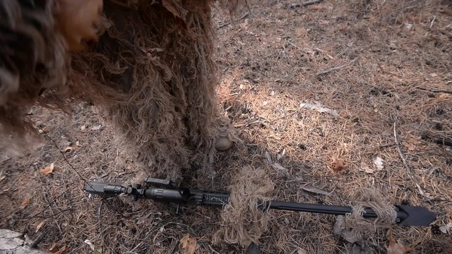 Sniper with large-caliber rifle in forestin / Sniper in camouflage suit with sniper rifle with scope in forest