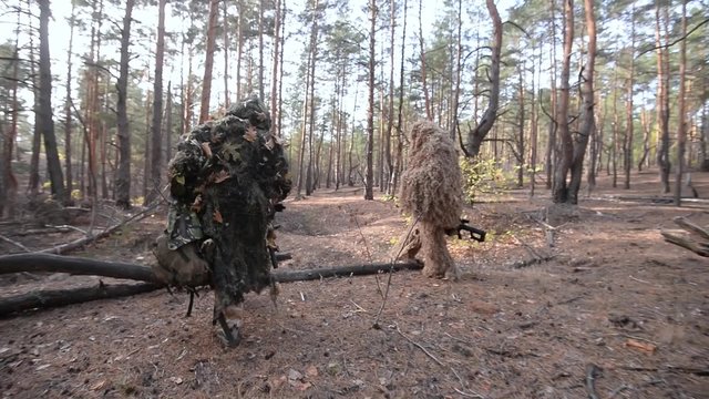 Two snipers go through the woods / Two sniper in camouflage suits going through the forest with rifles and backpacks