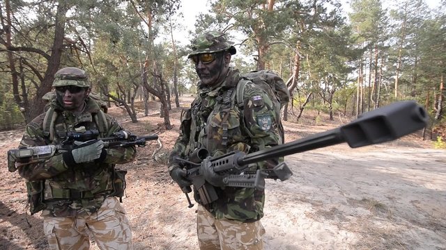 Two snipers with sniper rifles in hands/ Two armed soldiers with sniper rifles in forest during military operation 