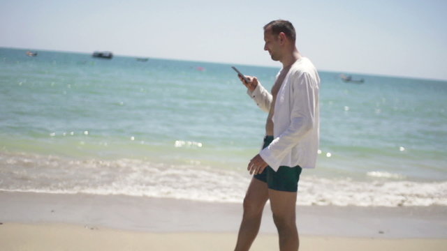 Young man using smartphone and walking on beach
