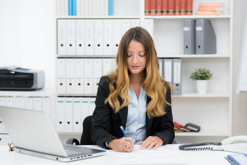 junge frau sitzt am arbeitsplatz und schreibt