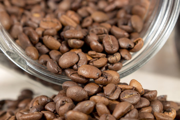 Close-up of roasted coffee beans that get out of an overturned and open glass pot