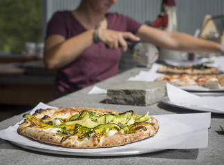 Obraz na płótnie Canvas Fresh Zucchini and Ricotta Pizza Just Out of the Oven: Fresh Zucchini and Ricotta Pizza just out of the oven on a counter with other pizzas and pizza cutter in background