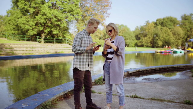 Couple using smartphones next to the river and smiling to the camera

