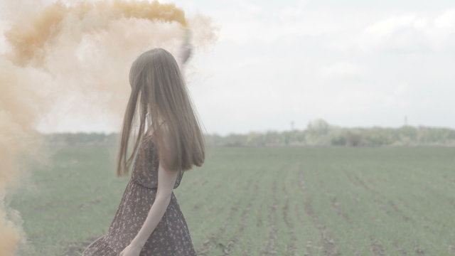 Happy young woman in dark dress with floral print having fun outdoor in geen field. Beauty girl with orange smoke bomb spinning and laughing. middle shot ungraded flat color