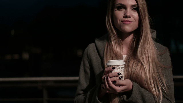 Girl teenager in the street at night drinking coffee and waiting