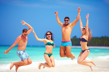 happy excited group of young friends jumping on summer beach