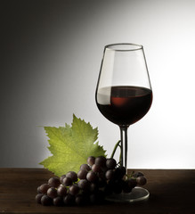 Glass with red wine and grapes on the wooden table