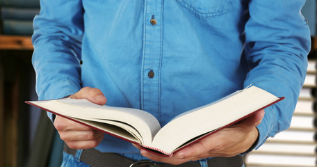 Male hands holding open book on bookshelves background