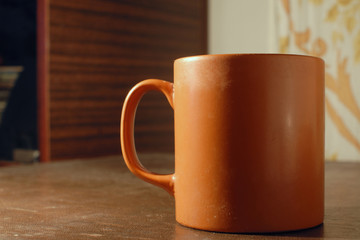 Orange cup with tea or coffee on the wooden table
