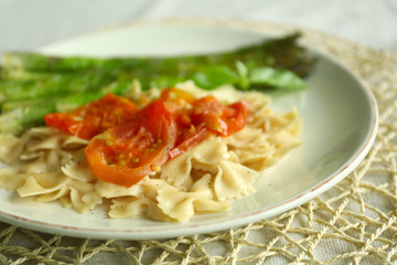 Roasted asparagus and tasty pasta with vegetables on plate on wooden table background