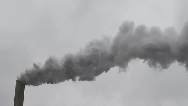 Thick smoke flowing out of a high factory chimney on a stormy day.
