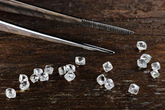echte Rohdiamanten mit Pinzette auf rustikalem Holzhintergrund
