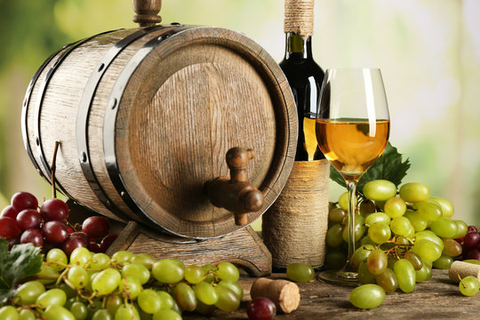 White and red grape with wine bottle near barrel on wooden table, close up