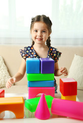 Little girl playing with cubes on home interior background