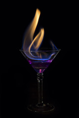 Martini glass with purple drink is on fire and very hot