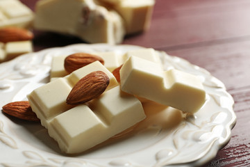White chocolate pieces with nuts on plate, on color wooden background
